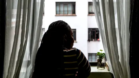 BBC/Shiraaz Mohamed A Zimbabwean woman looking out of a window in Hillbrow, Johannesburg, South Africa