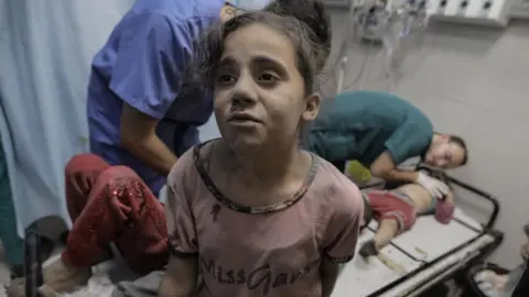 Getty Images little girl covered in dust standing in front of a hospital bed at Nasser Medical Hospital on November 16, 2023 in Khan Yunis, Gaza.
