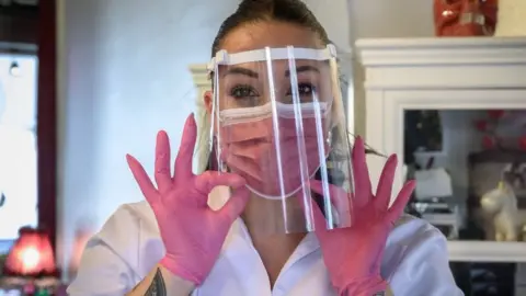 Getty Images Beauty salon owner in Lausanne, Switzerland wearing gloves, mask and a visor