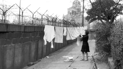 A woman hangs washing on the Berlin Wall