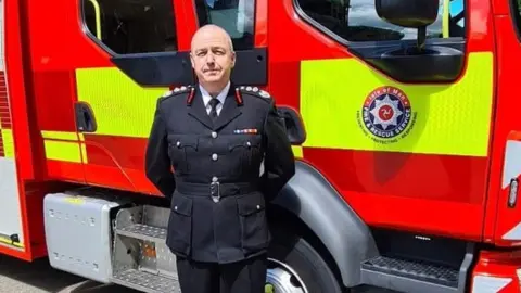 IOM GOVERNMENT Mark Christian standing in front of a fire engine