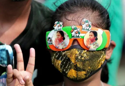 EPA A Trinamool Congress party (TMC) supporter wears glasses with pictures of party supreemo Mamata Bannerjee and shows victory sign as they celebrate after winning an absolute majority in the West Bengal Assembly Election in Kolkata, India, 02 May 2021
