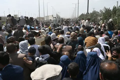 AFP Afghans gather on a roadside near the military part of the airport in Kabul on August 20, 2021, hoping to flee from the country after the Taliban's military takeover