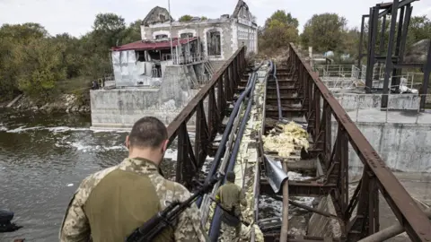 Getty Images Ukrainian soldiers cross damaged bridge in the recaptured town of Velyka Oleksandrivka in Kherson region,