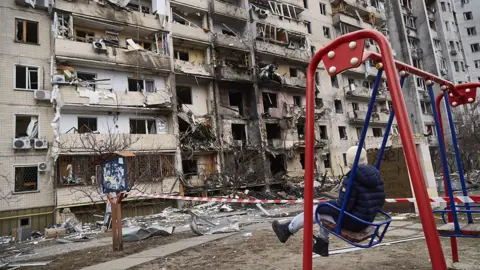 Getty Images A child on a swing outside a residential building damaged by a missile on February 25, 2022 in Kyiv, Ukraine.