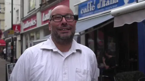 Man in white shirt and glasses stands outside coffee shop