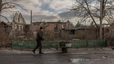 Getty Images A man pushes a trolley with a coal container to his flat, passing war-damaged buildings