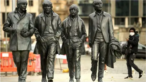 Getty Images Man in face mask walking behind statue of the Beatles in Liverpool