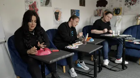 In a craft workshop women paint masks with contrasting gambling and gamble-free faces