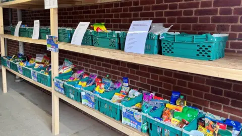 Helen Mulroy/BBC Food bank aisle with crates of products