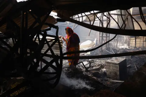 MOHAMMAD PONIR HOSSAIN/Reuters Sondhya Baidya stands in burned down building after a fire that broke out at the Mohammadpur Krishi Market in Dhaka, Bangladesh, September 14, 2023.