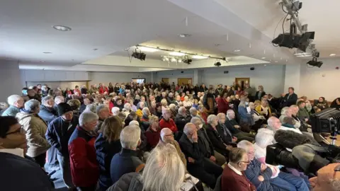 BBC People sitting in a hall to discuss the closure of their GP surgery