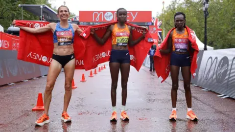 Getty Images First place Brigid Kosgei of Kenya, second place Sara Hall of The United States of America and third place Ruth Chepngetich of Kenya pose for a photo following competing in the Elite Women's Field during the 2020 Virgin Money London Marathon