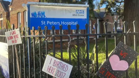 Simon Dedman/BBC Railings outside a Victorian hospital building with placards including "I was born here"