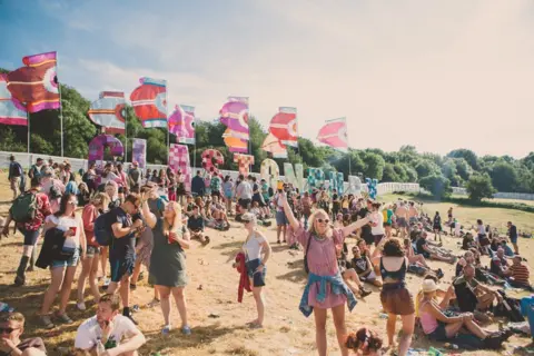 Emma Stoner Crowd of people at Glastonbury Festival 2017, with flags and trees in the distance