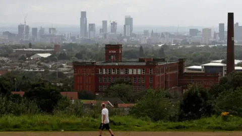 Reuters Manchester city centre in background, Oldham in foreground with man walking past