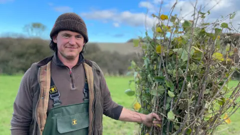 Jake Greenfield in a field holding branches