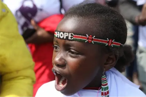 EPA A girl wearing a beaded headband with the word "hope" weaved into is seen shouting. Her expression is passionate.