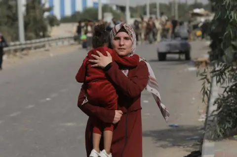 BBC A mother fleeing with her child on the Salah al-Din road, which was bombed on Friday.