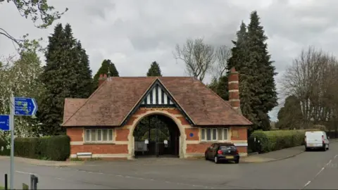 Google Single-storey brick building with archway entrance. There are tall trees on either side
