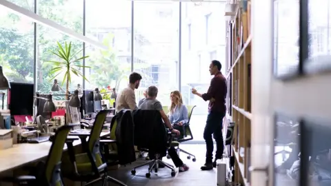 Getty Images business people discussing in office. Male and female professionals are working together at workplace. They are wearing smart casuals.