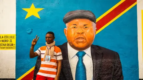 Getty Images A supporter of veteran opposition chief Etienne Tshisekedi poses for a photograph with his portrait front of his residence in Kinshasa, on July 27, 2016. Etienne Tshisekedi,