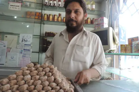 BBC Ahmar Mehmood a.k.a. Ahmar Badayuni (sic), and a tray of Badauni pedhe - taken inside Badauni Pedha House, Bank Road, Mardan
