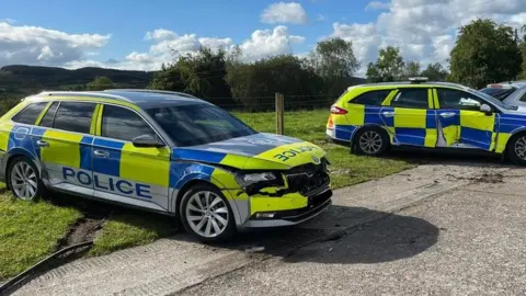 Three police cars showing damage after being rammed by tractor