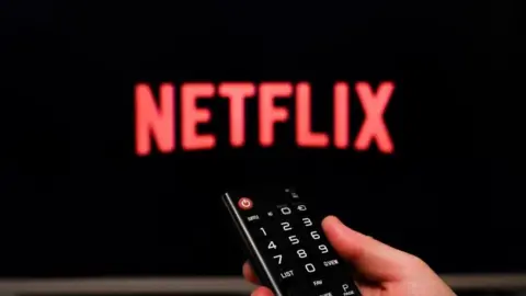 Getty Images Netflix logo on a TV with hand holding remote