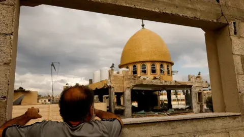 Reuters A Palestinian man looks at a mosque damaged in an Israeli air strike in Khan Younis, in the southern Gaza Strip (15 November 2023)