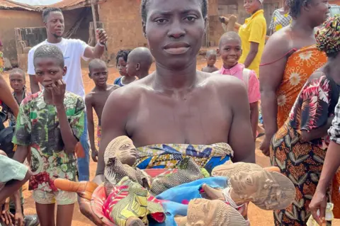 BBC/Alex Last A woman hold figurines used at the shrine for twin gods in Igbo-Ora, Nigeria