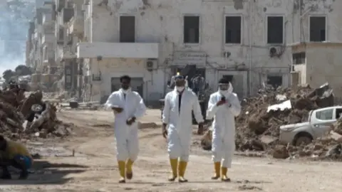 Men in hazmat suits walking through Derna