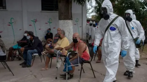 AFP/Getty Images Brazilian soldiers in protective suits prepare to disinfect a public shelter in Rio de Janeiro. Photo: May 2020