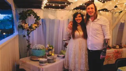 Jae and Rayna Harvey Rayna and Jae pictured on their wedding day with Jae in a white dress and Rayna in a white shirt and trousers