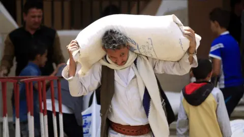 AFP A man carries food aid from the UN's World Food Programme in Sanaa, Yemen (26 June 2018)