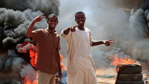 AFP Sudanese demonstrators flash victory signs by a roadblock made of buring tyres in the capital Khartoum, on October 26, 2021, as they protest a military coup that overthrew the transition to civilian rule