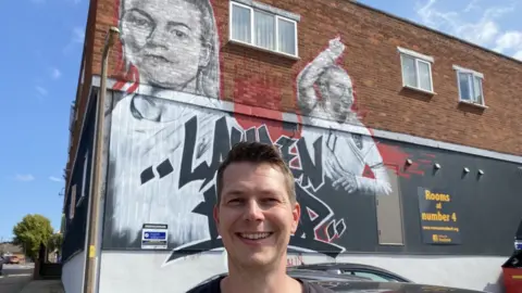 Chris Taylor in front of the town's Lauren Hemp mural