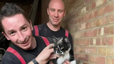 Dunstable Community Fire Station  Two firefighters with a cat they have rescued from a wall