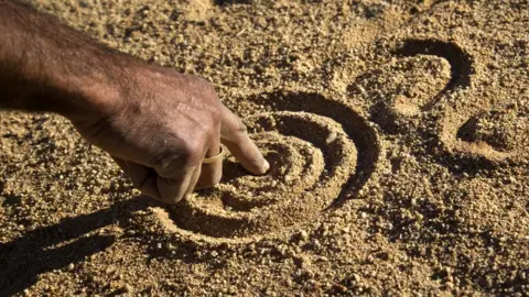 Getty Images A close up of an Aboriginal man's hand drawing the dreamtime stories in the dirt