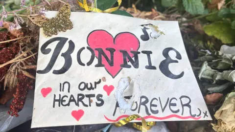 A card with a love heart says 'Bonnie in our hearts forever'
