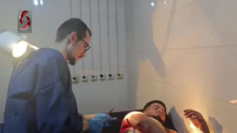 Al-Ikhbariya al-Suriyah TV Syrian state-run Al-Ikhbariya al-Suriyah TV footage shows a doctor treating a man injured in a suspected Israeli strike at a hospital in Masyaf, Syria (9 September 2024)