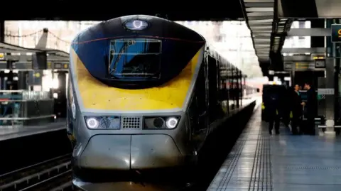 A train at a train station. The train is yellow on the front with blue sides.