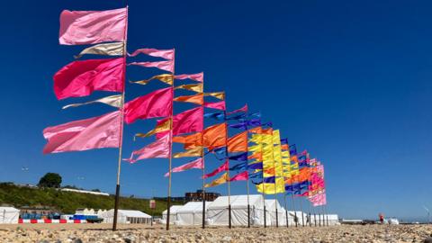Multi-coloured flags ripple in the breeze in front of white marquees at Lowestoft beach