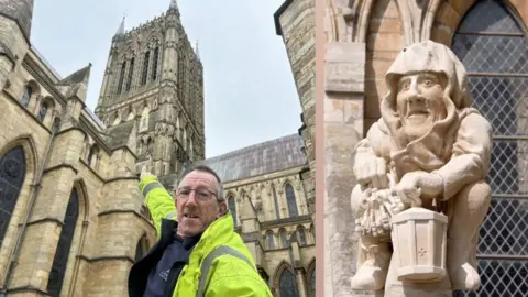 BBC/Lincoln Cathedral A composite image of two photos. On the left is a man wearing a yellow high-vis coat and rectangular glasses smiling into the camera as he points up at a statue on a cathedral. On the right is a close-up of the statue in a medieval style, showing a man in a sitting position holding keys and a lantern with a hooded shroud over his head. The window of a cathedral can be seen behind it.