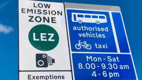 A low emission zone sign. One side says "Low Emission Zone" with the picture of a camera and the other side says "authorised vehicles" with an image of a bus and a bike.