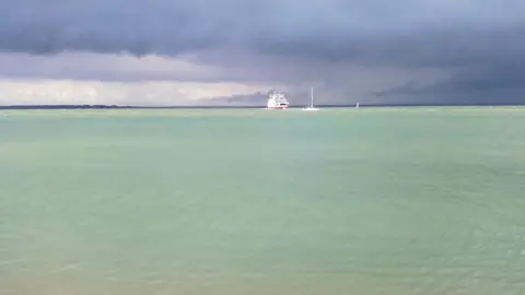 madpenguin The view from Cowes on the Isle of Wight over the Solent. The sea water is a light green and above the sky is dark grey clouds. You can see a Red Funnel ferry in the distance and a small white yacht.
