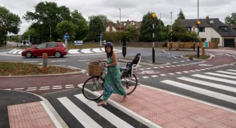 A woman pushing a bike across a zebra crossing
