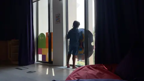 Eight-year-old Azuriah staring out of a window. The boy is pictured from the back and there is a card design on one of the long windows. 