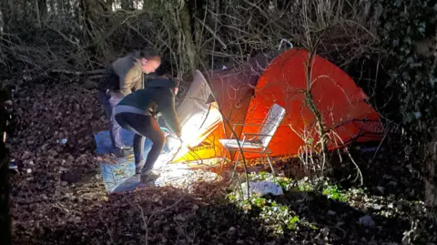 Harriet and Richard are checking inside an orange tent 