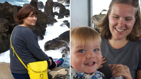 A woman sitting above a rocky sea turning to look over her shoulder and a second woman smiling at a toddler who is turning to look at the camera